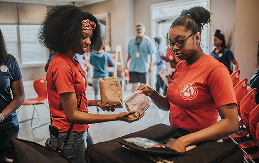 A person handing a packaged Chick-fil-A Chicken Sandwich to another person