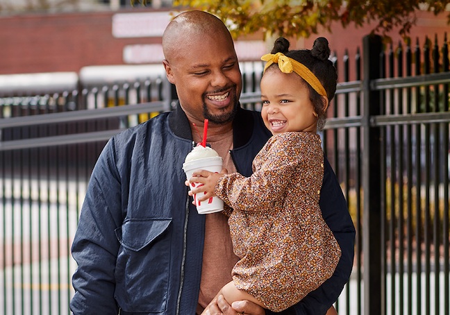 Man holding a little girl who is holding a Chick-fil-A milkshake