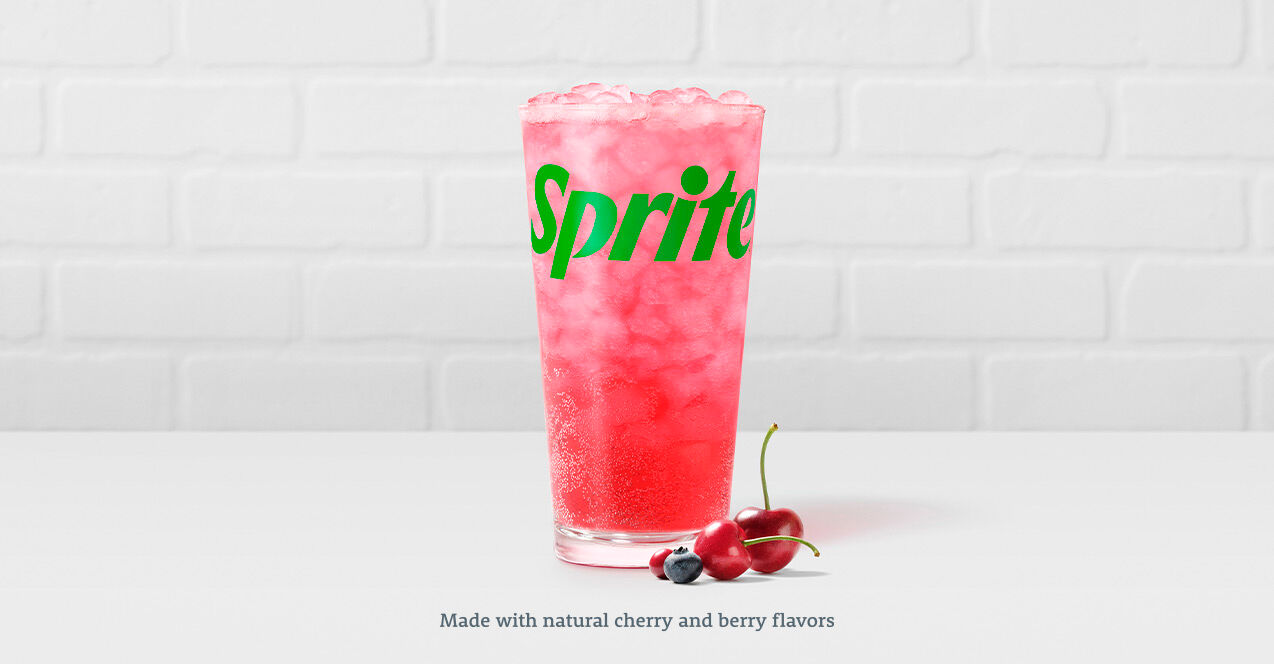 A glass of Cherry Berry & Sprite® with cherries and berries sitting in front of it