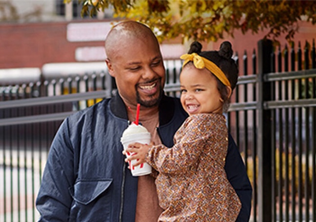 Adult holding a child who is holding a Chick-fil-A milkshake and both of them are smiling