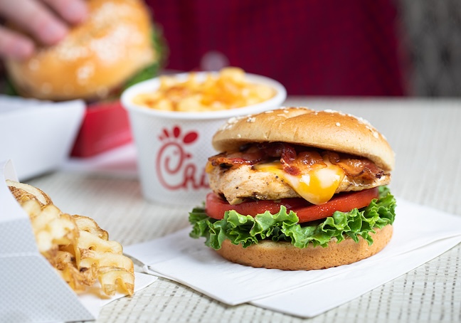 Grilled Chicken Sandwich on a napkin on a table with a Mac & Cheese and Waffle Fries next to it