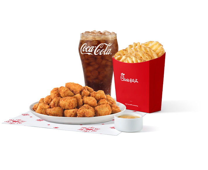 30-ct Chick-fil-A Nuggets sitting on holiday-themed parchment paper next to a glass of Coke Zero and a carton of Waffle Fries