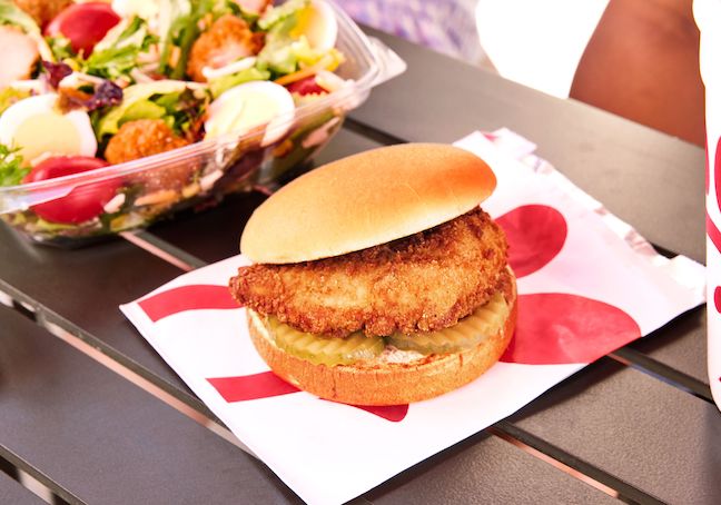 Chick-fil-A® Chicken Sandwich sitting on its packaging on a table next to a Cobb Salad