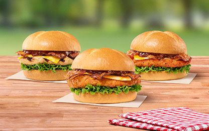 Smokehouse BBQ Bacon Sandwich with Grilled filet, Smokehouse BBQ Bacon Sandwich with Original filet, Smokehouse BBQ Bacon Sandwich with Spicy filet sitting on a table next to a red and white napkin with grass and trees in the background