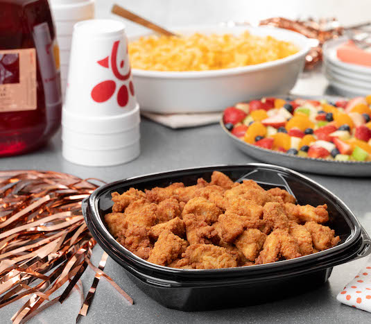 Chick-fil-A Nugget Tray with Fruit Tray and Mac & Cheese Tray on table with gallon of Iced Tea, cups and decorative streamers