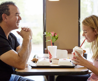 Man and girl sitting at a table, eating and drinking Chick-fil-A food