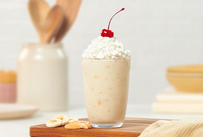 A Banana Pudding Milkshake on a brown dish with banana slices and wafers