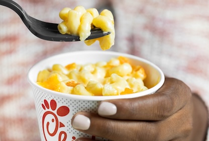 Person holding a cup of Mac & Cheese, raising a fork out of it 