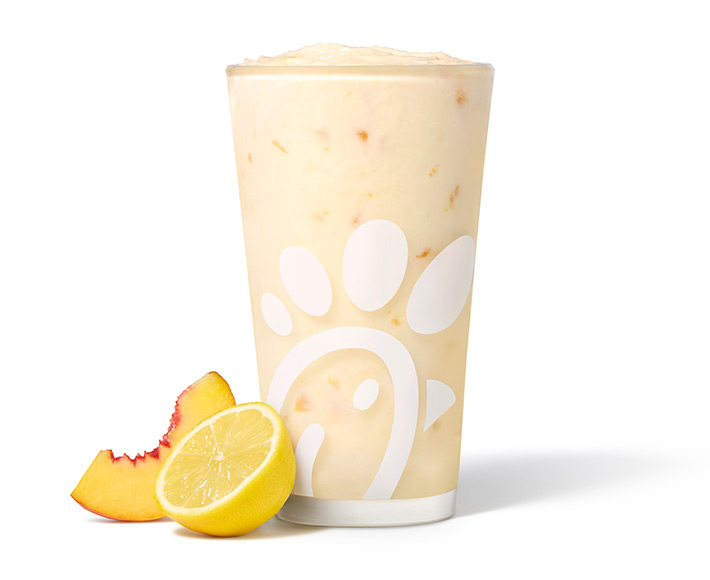A glass of Peach Frosted Lemonade with a peach slice and a lemon half