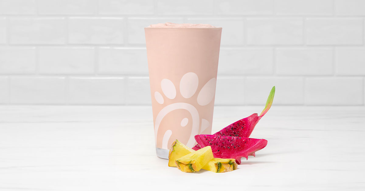 A glass of a Pineapple Dragonfruit Frosted Lemonade with pieces of pineapple and dragonfruit next to it on a tiled background