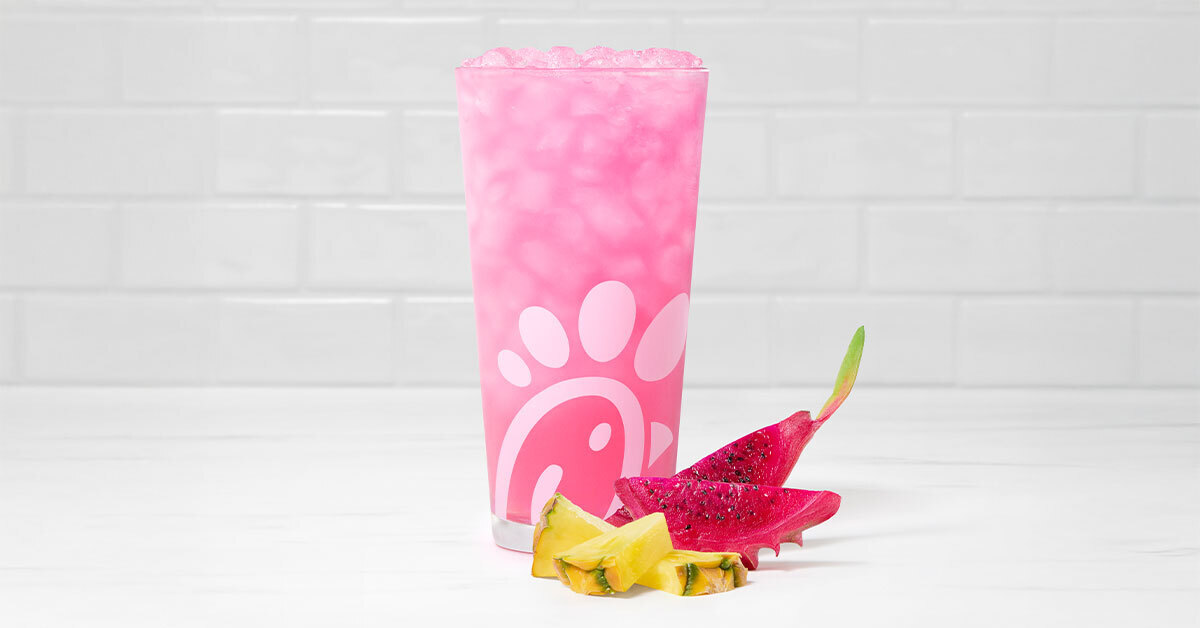 A glass of a Pineapple Dragonfruit Lemonade with pieces of pineapple and dragonfruit next to it on a tiled background