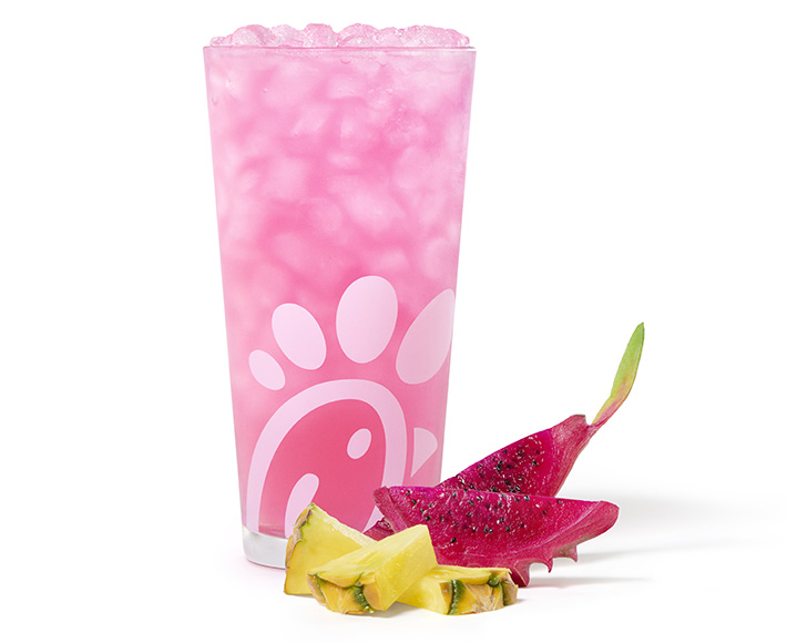 A glass of a Pineapple Dragonfruit Lemonade with pieces of pineapple and dragonfruit next to it on a tiled background