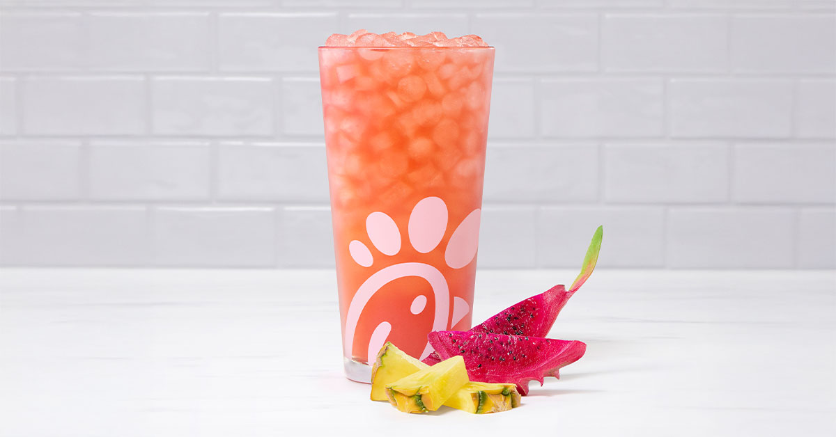 A glass of a Pineapple Dragonfruit Sunjoy® with pieces of pineapple and dragonfruit next to it on a tiled background