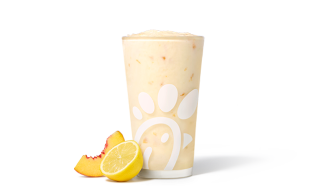 A glass of Peach Frosted Lemonade with a peach slice and a lemon half