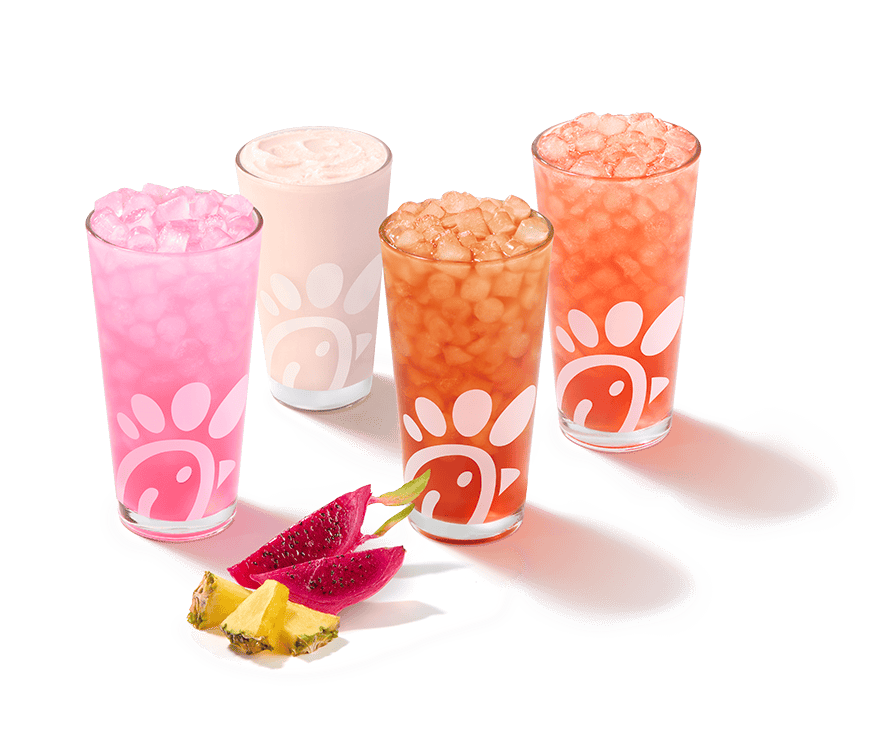 Angled photo of a glass of a Pineapple Dragonfruit Lemonade, Frosted Lemonade, Iced Tea and Sunjoy® with pieces of pineapple and dragonfruit next to them on a white background