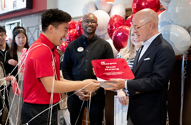 Chick-fil-A CEO Andrew Cathy hands a large, symbolic sauce packet to Noel H., a Chick-fil-A Team Member and 2024 True Inspiration Scholarship recipient