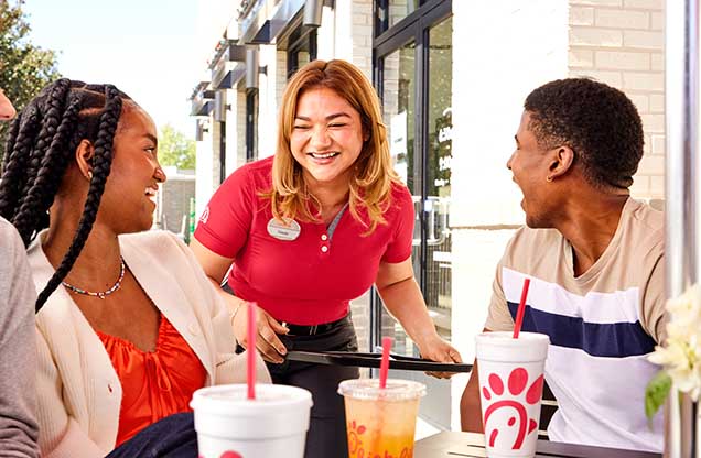 Chick-fil-A® Team Member bringing food to two customers sitting outside