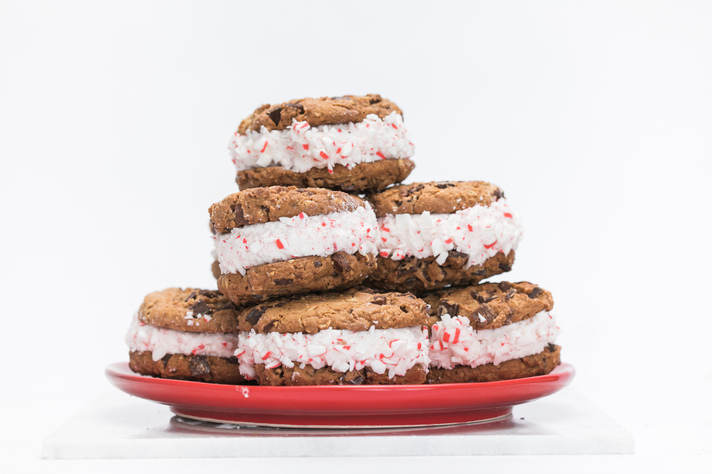 Peppermint ice cream cookie sandwiches made with Chick-fil-A Chocolate Chunk Cookies stacked on a red plate. 