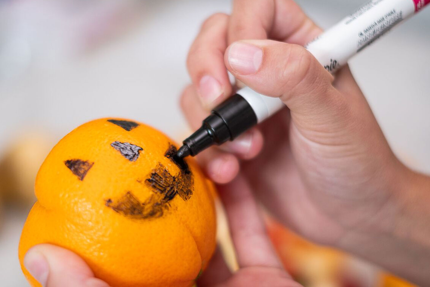 Person drawing a jack-o'-lantern face on the outside of the mandarin orange