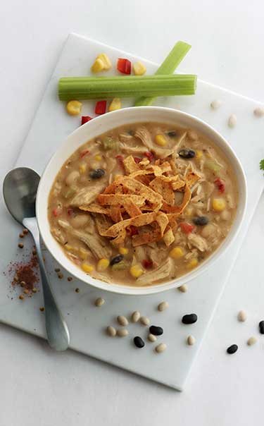 Bowl of Chick-fil-A Chicken Tortilla Soup surrounded by beans, corn, celery and a spoon. 
