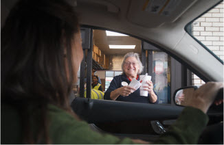 Chick-fil-A Team Member handing a drink to another person inside a car