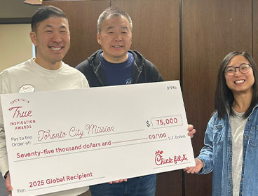 Three people from Toronto City Mission standing together, holding a large check and smiling
