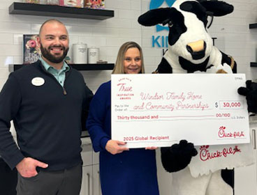 Two people from Windsor Family Home and Community Partnerships standing together with a Chick-fil-A Cow, holding a large check and smiling