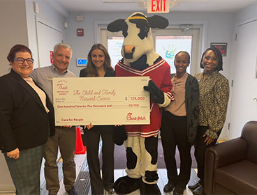 A Chick-fil-A Cow holding a large check with people from the Child and Family Network Centers organization standing around him and smiling
