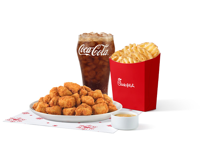 Chick-fil-A Nuggets de 30 en un plato blanco junto a una salsa para mojar, Waffle Fries y un vaso de Coca Cola  en un fondo blanco